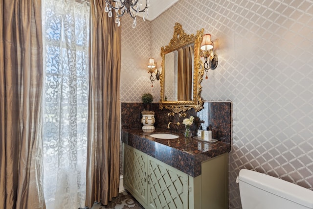 half bathroom featuring toilet, a chandelier, vanity, and wallpapered walls