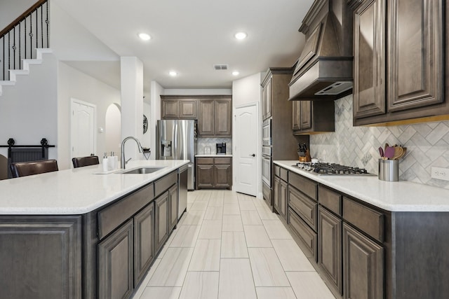 kitchen featuring visible vents, premium range hood, dark brown cabinetry, appliances with stainless steel finishes, and a sink