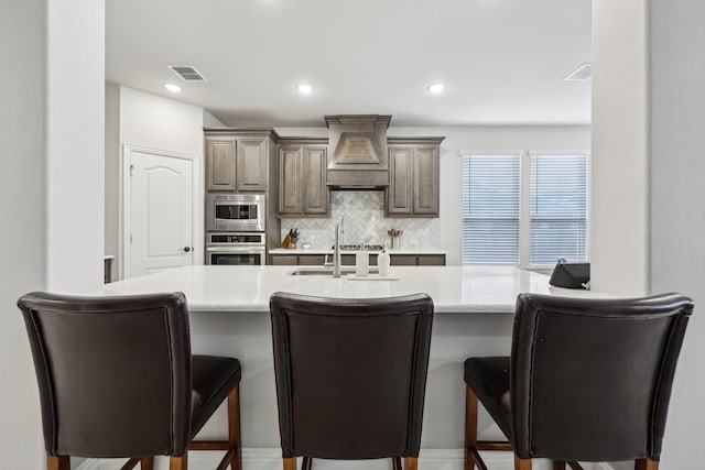 kitchen with backsplash, light countertops, a kitchen breakfast bar, custom exhaust hood, and stainless steel appliances