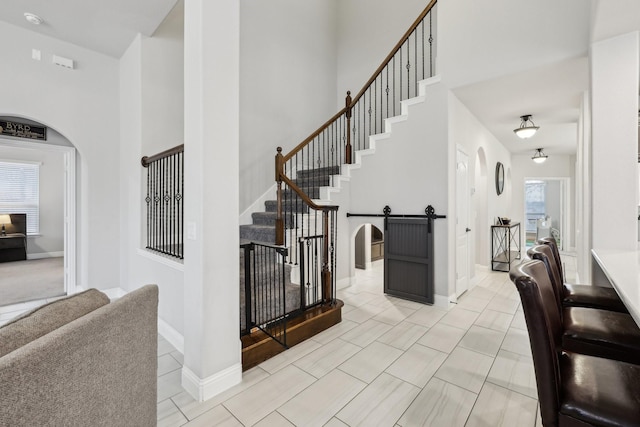 staircase with arched walkways, tile patterned flooring, baseboards, and a towering ceiling