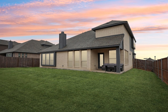 rear view of property featuring a patio, a lawn, brick siding, and a fenced backyard