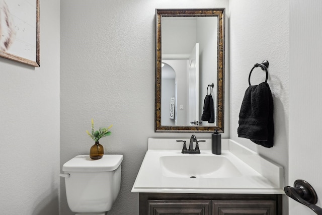 half bathroom featuring vanity, toilet, and a textured wall