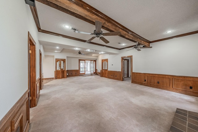 unfurnished living room featuring visible vents, beam ceiling, light carpet, a textured ceiling, and wainscoting