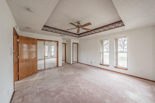 unfurnished room featuring a wealth of natural light, light carpet, a raised ceiling, and baseboards