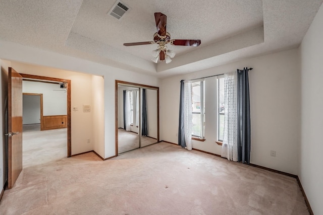 unfurnished bedroom with a textured ceiling, a raised ceiling, and light carpet