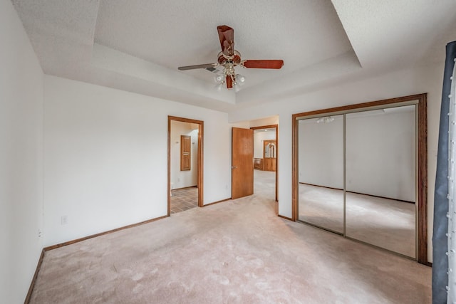 unfurnished bedroom with baseboards, a tray ceiling, a closet, a textured ceiling, and light colored carpet