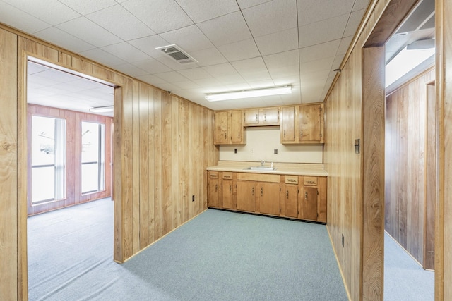 kitchen featuring visible vents, carpet floors, a sink, light countertops, and wood walls