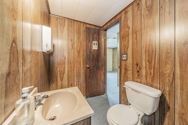 half bath with wooden walls, toilet, and vanity