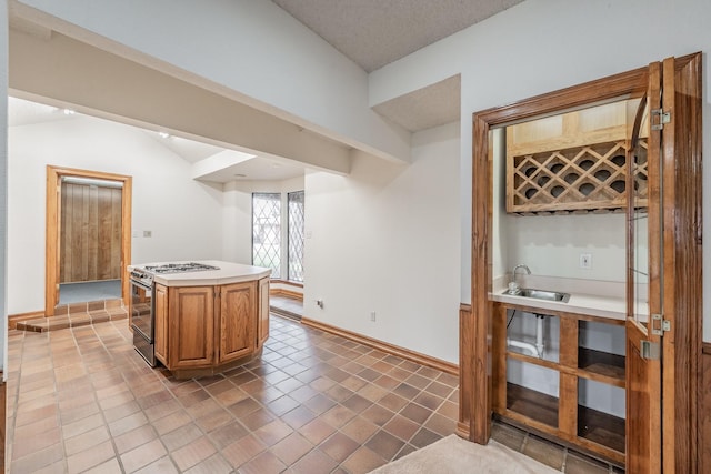 kitchen with a sink, a kitchen island, gas stove, light countertops, and baseboards