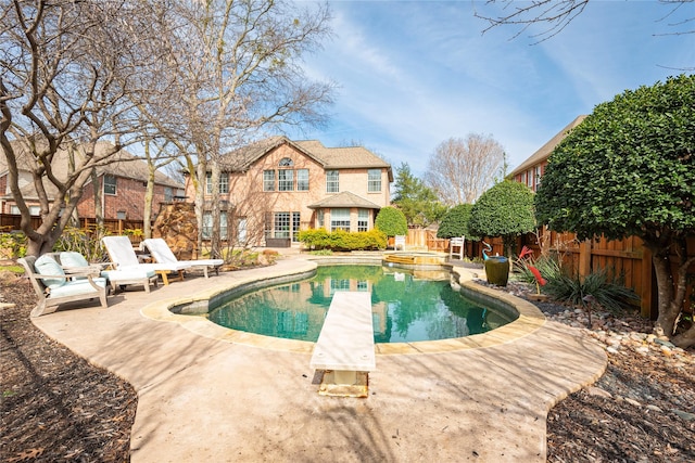 view of swimming pool featuring a pool with connected hot tub, a patio area, a diving board, and a fenced backyard