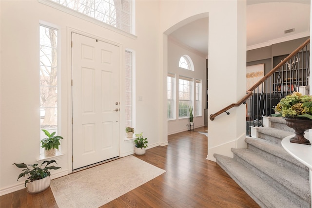 foyer featuring wood finished floors, visible vents, arched walkways, a towering ceiling, and crown molding