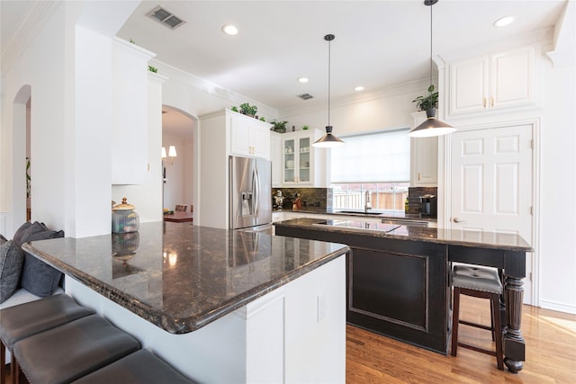 kitchen with a kitchen breakfast bar, stainless steel fridge, arched walkways, and light wood-style flooring