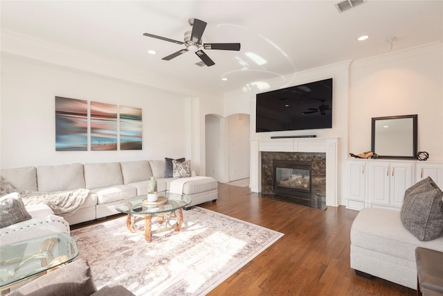 living area with wood finished floors, visible vents, arched walkways, a high end fireplace, and crown molding