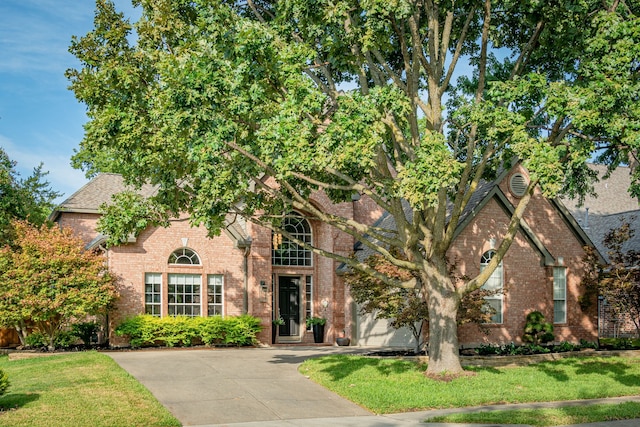 view of front facade with brick siding, driveway, and a front lawn