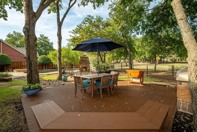 wooden deck with outdoor dining space, an outdoor stone fireplace, and a fenced backyard