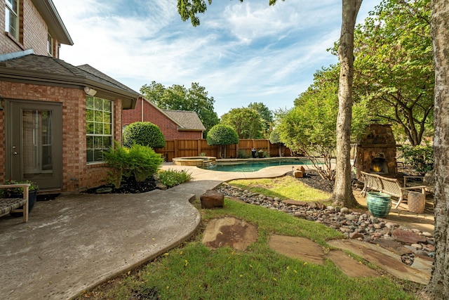 view of yard with a patio, a fenced backyard, a pool with connected hot tub, and an outdoor stone fireplace