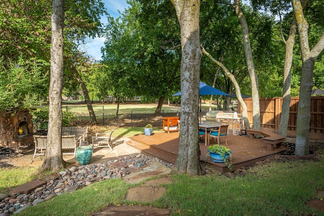 view of yard with a wooden deck, an outdoor stone fireplace, and fence