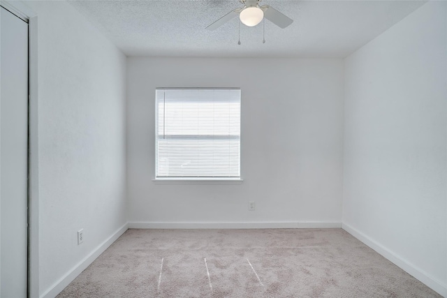 carpeted spare room featuring baseboards, a textured ceiling, and a ceiling fan