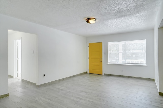 empty room with baseboards, a textured ceiling, and light wood-style flooring