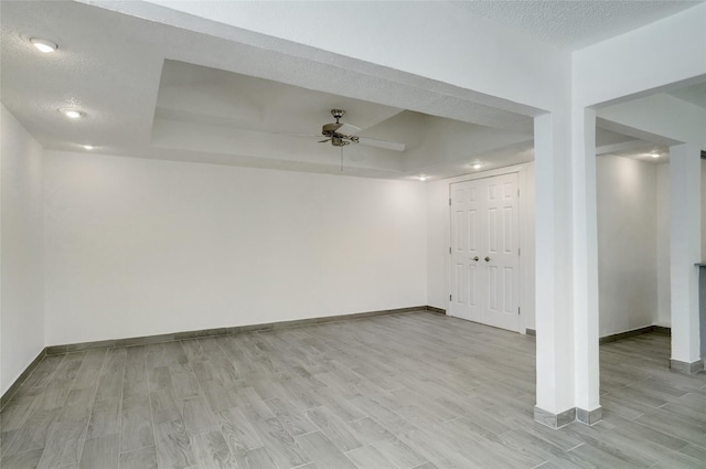 basement with a textured ceiling, light wood-type flooring, and baseboards