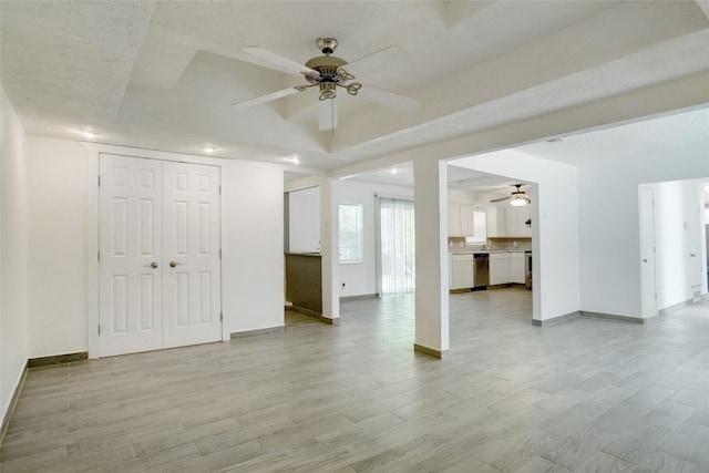 unfurnished living room with light wood-style flooring, baseboards, a tray ceiling, and ceiling fan