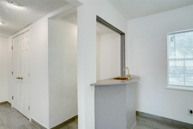 interior space with a healthy amount of sunlight, a textured ceiling, baseboards, and a sink