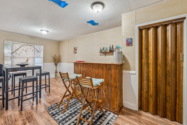 bar featuring a textured ceiling, wood finished floors, wainscoting, and a dry bar