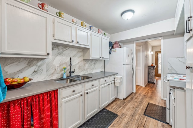 kitchen with backsplash, freestanding refrigerator, light wood-style floors, white cabinets, and a sink