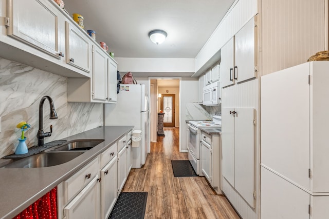 kitchen with light wood-type flooring, a sink, backsplash, white appliances, and white cabinets