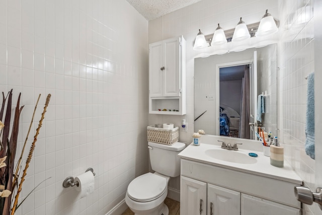 bathroom featuring vanity, tile walls, toilet, and a textured ceiling