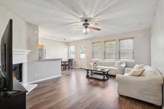 living room featuring dark wood-style floors, baseboards, a ceiling fan, a textured ceiling, and a glass covered fireplace