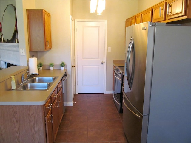 kitchen with dark tile patterned floors, light countertops, appliances with stainless steel finishes, brown cabinetry, and a sink