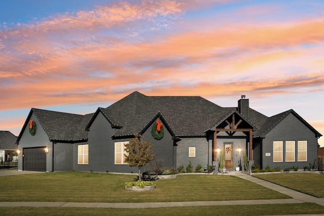 view of front facade with a lawn, driveway, an attached garage, brick siding, and a chimney