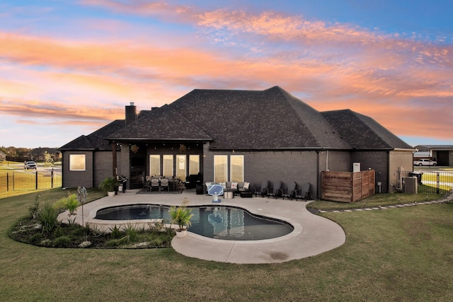 back of property at dusk featuring a lawn, a patio, fence, a fenced in pool, and a chimney