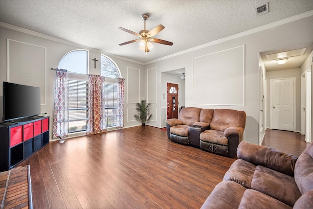 living area with visible vents, ornamental molding, a ceiling fan, a decorative wall, and dark wood-style flooring