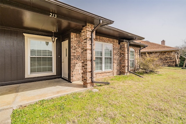 view of exterior entry with brick siding and a yard