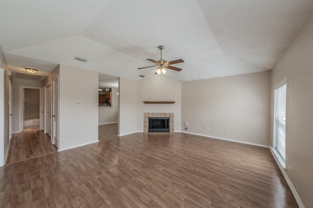 unfurnished living room with visible vents, a tiled fireplace, vaulted ceiling, wood finished floors, and a ceiling fan