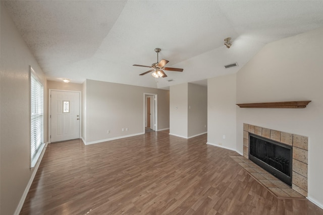 unfurnished living room featuring a tiled fireplace, visible vents, wood finished floors, and vaulted ceiling