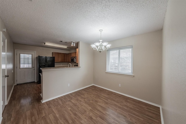 kitchen featuring stainless steel microwave, black fridge, a notable chandelier, a textured ceiling, and dark wood-style flooring