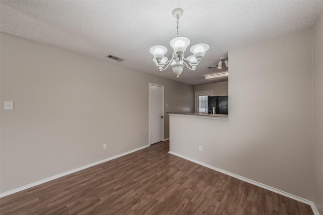 empty room featuring visible vents, baseboards, dark wood finished floors, a notable chandelier, and a textured ceiling