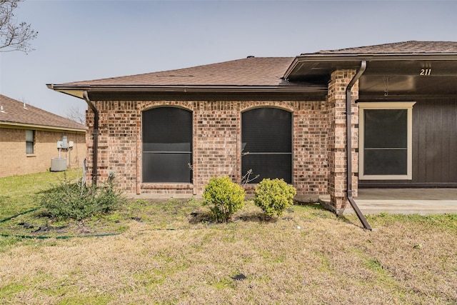 view of front facade with brick siding, central AC, a front lawn, and a patio