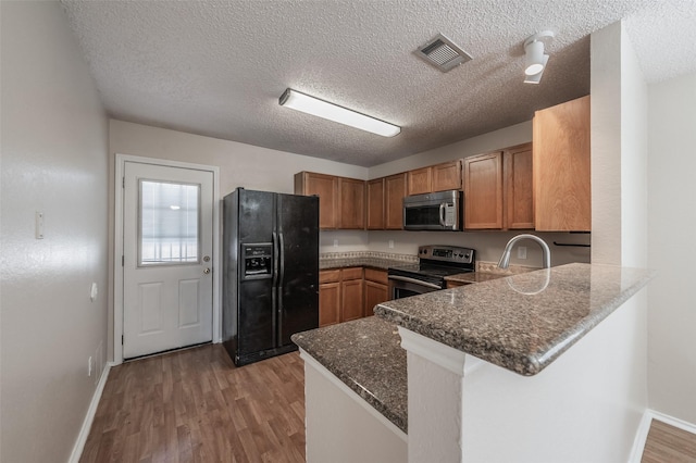 kitchen featuring light wood finished floors, visible vents, dark stone counters, appliances with stainless steel finishes, and a peninsula