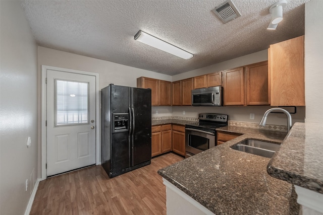 kitchen featuring visible vents, brown cabinets, light wood-style floors, stainless steel appliances, and a sink