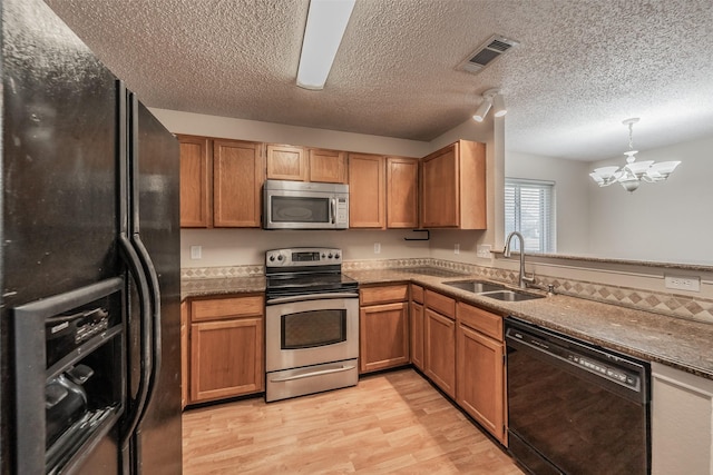 kitchen featuring visible vents, a sink, black appliances, a notable chandelier, and light wood-type flooring