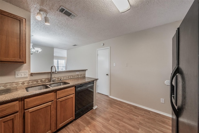 kitchen with light wood finished floors, visible vents, brown cabinets, black appliances, and a sink