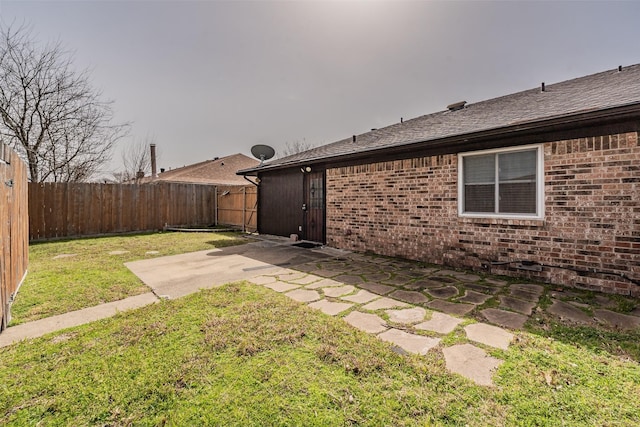 exterior space with brick siding, roof with shingles, a lawn, a fenced backyard, and a patio