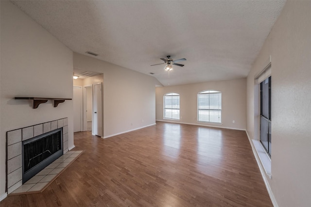 unfurnished living room with visible vents, a tiled fireplace, wood finished floors, baseboards, and ceiling fan