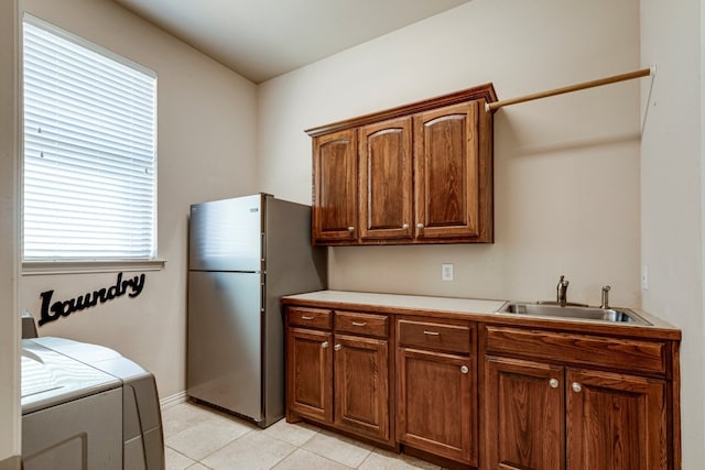 kitchen featuring independent washer and dryer, a sink, freestanding refrigerator, light tile patterned flooring, and light countertops