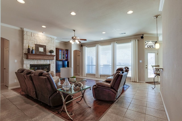 living area with arched walkways, a stone fireplace, and ornamental molding