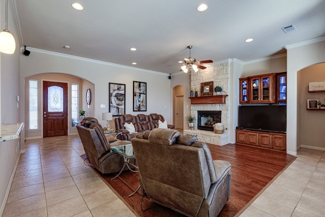 living room featuring recessed lighting, a stone fireplace, ornamental molding, and light tile patterned floors